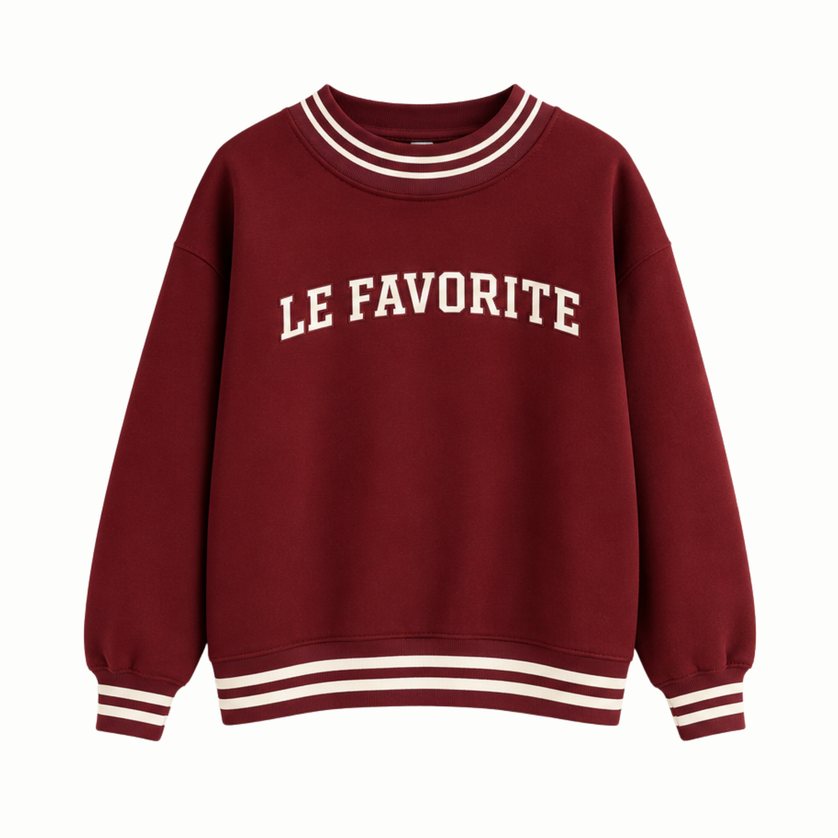 A maroon crewneck sweatshirt with 'LE FAVORITE' printed in cream arched lettering across the chest, featuring cream double-stripe accents on the collar, cuffs, and hem.